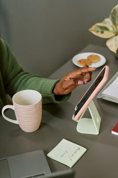 Vertical shot of Black woman using tablet at desk, managing digital tasks and schedule during workday. Suitable for remote work, productivity, planning, or business app marketing