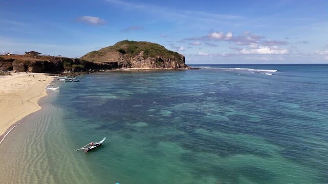Aerial view flying over a stunning tropical coastline with crystal clear turquoise water, a sandy beach, fishing boats, and a rocky headland, perfect for a peaceful travel destination