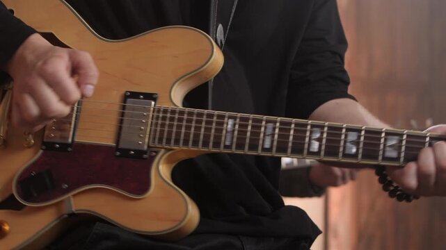 Close-up of a guitarist's hands playing chords and strumming a semi-hollow electric guitar during a live performance, with the camera panning along the fretboard towards the headstock