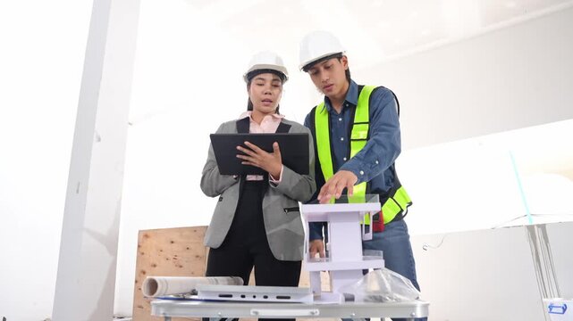 Asian engineer working and female architect reviewing architectural plans and examining a building model at a renovation or construction site