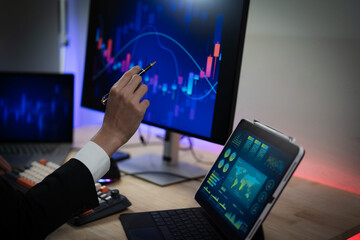 Fototapeta premium Business professionals are analyzing investment charts on their office computers at night, using digital tablet technology to analyze market growth.