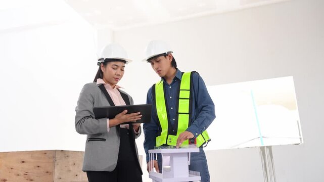 Asian engineer working and female architect reviewing architectural plans and examining a building model at a renovation or construction site