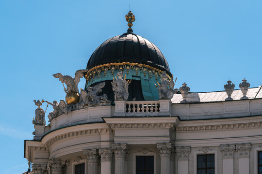 View of the ornate dome of the Hofburg Palace featuring intricate sculptures and gold detailing against a clear blue sky in Vienna, Vienna, Austria.