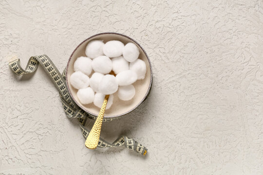 Bowl of cotton balls with fork and measuring tape on grunge white background. Unhealthy diet concept
