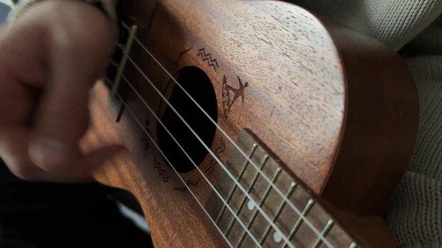 Man plucking ukulele strings close up at home, playing melody, music practice session, creative hobby activity, musical performance