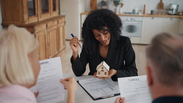 Presentation of real estate, woman broker talking with clients, discuss project. African american lady showing model of new living house and explaining conditions of installment plan and credit
