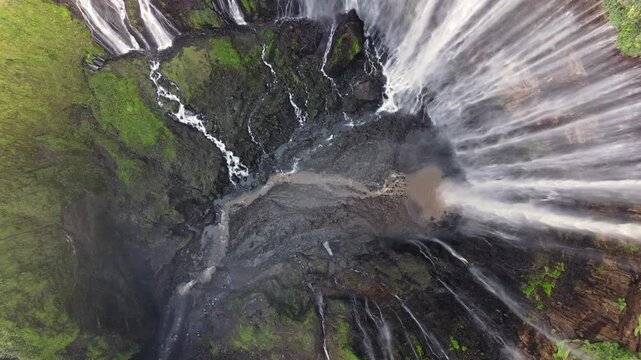 Drone rises from low ground near Tumpak Sewu building dramatic tension before revealing the breathtaking full scale and raw power of the waterfall East Java Indonesia