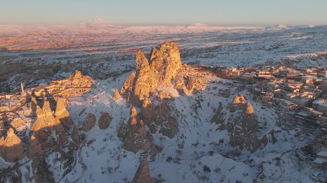 Aerial drone tilt up reveal of Uchisar castle snowy peak landscape at sunset