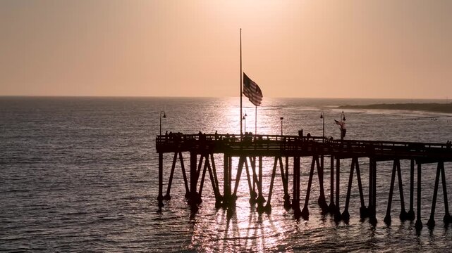 American flag at half mast symbolizing mourning, remembrance, and national respect. Patriotic Unites States of America flag lowered on flagpole with golden sunset background. RIP Charlie Kirk