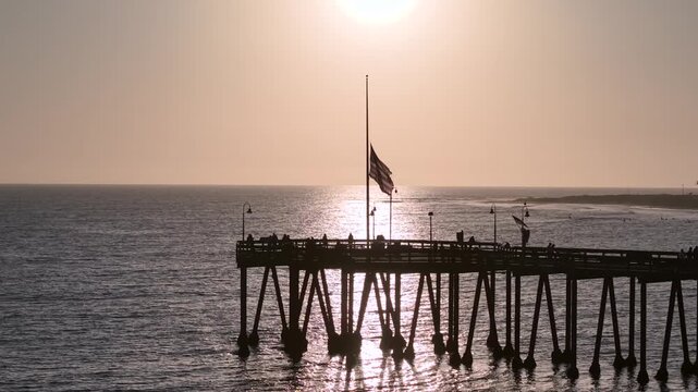 American flag at half mast symbolizing mourning, remembrance, and national respect. Patriotic Unites States of America flag lowered on flagpole with golden sunset background. RIP Charlie Kirk
