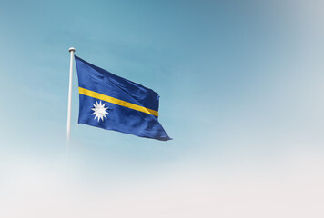 Fototapeta premium Nauru national flag with mast waving in beautiful sky. Nauru flag for Republic Day and Independence Day.