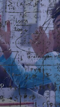 Vertical video: Boy touching transparent pane tracing math pointing to peer solving classroom task