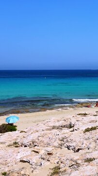 Sunny summer day, Ses Illetes Beach, vertical pan shot, yatch on turquoise sea, pristine white sand, beachgoers, Formentera Island, Spanish travel destination.