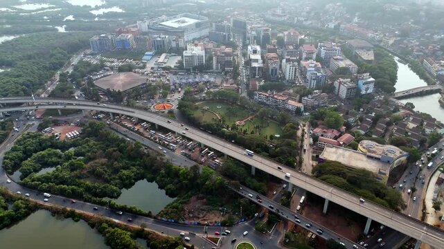 Cinematic aerial view of Panaji showcasing a modern urban landscape with elevated highways, the city's bus station, busy intersections, and a dense cluster of buildings fading into a hazy horizon.