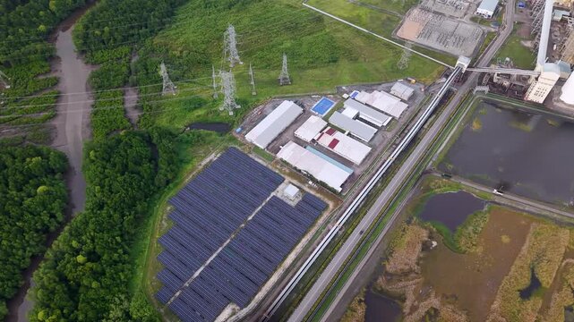 Top-down drone shot of solar array adjacent to transmission towers, power plant, wetlands and roads.