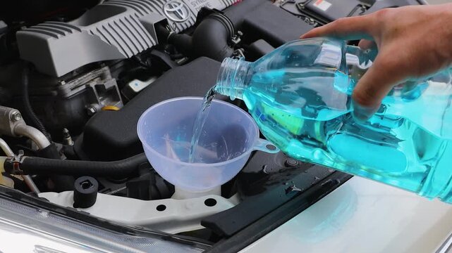 自動車のボンネットを開けてウィンドウォッシャー液を補充している	