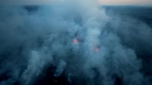 Aerial drone captures smoldering peat fire and thick smoke over dark marshland at dusk.