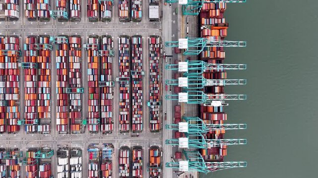Top down drone view of colorful stacked shipping containers and cranes at busy port terminal