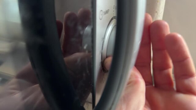 Person turning microwave control knob close up at home, setting time or power level, kitchen appliance use, cooking process concept