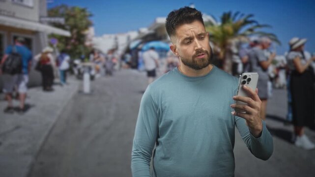 Man holding smartphone in right hand, looking at screen with a puzzled expression amid a crowded tourist street lined with palm trees and sunlit buildings; confusion travel.