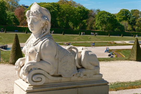 View of a white stone sphinx statue in the gardens of Belvedere Palace with manicured lawns and people in Vienna, Vienna, Austria.