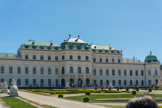 View of the Upper Belvedere Palace with its baroque architecture and green copper roofs overlooking manicured gardens and people walking under a clear blue sky in Vienna, Vienna, Austria.