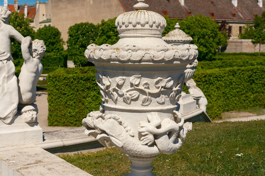 View of an ornate stone garden vase featuring intricate carvings of sea creatures and foliage at the Belvedere Palace gardens with cherub statues and manicured hedges Vienna, Vienna, Austria.