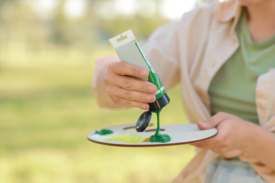 Female artist squeezing paint onto palette in park, closeup