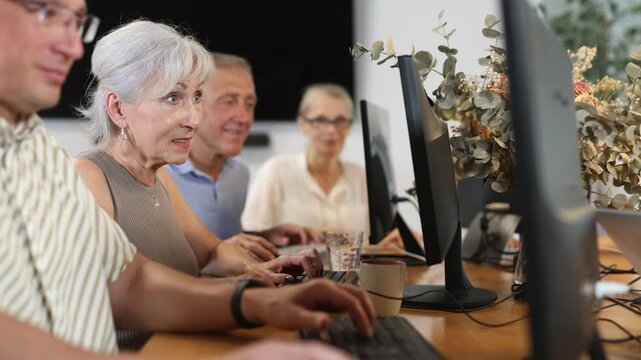 Interested positive elderly woman using computer to surf internet in library. Concept of integration of older generations with modern technology