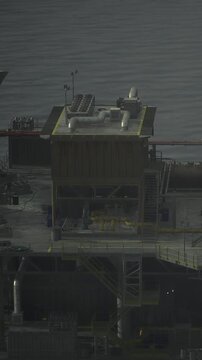 A tall oil platform stands above ocean water with multiple structures. The platform has equipment and pipes visible on its upper levels. The weather appears overcast and gray.