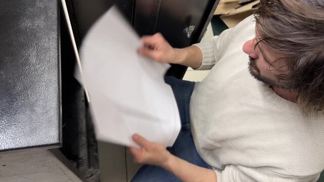 Man sorting through paper sheets, searching documents in archive, office and paperwork handling concept, indoor activity with files and records