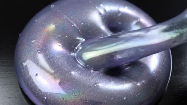 Close-up female hand with silver manicure pressing shiny purple glitter slime on black tabletop, concept of sensory relaxation and antistress play. asmr