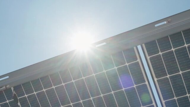 Bifacial solar panels generate clean energy with dual sided technology. Back view of photovoltaic modules under bright sun flare at industrial power farm for renewable electricity supply.