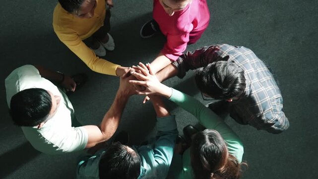 Top down view of smart business team working together and putting hands together. Aerial view of group of skilled business people brainstorming and making stack of hands at meeting room. Symposium.