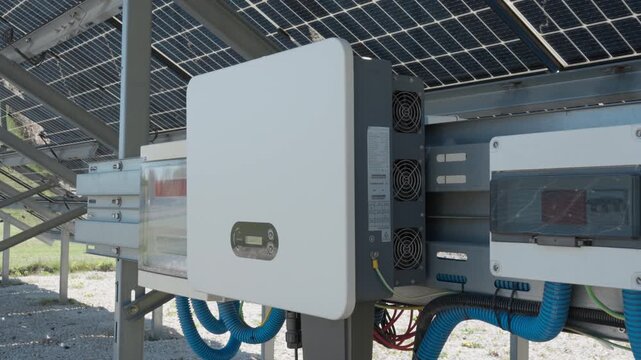 Industrial solar inverter converts energy from bifacial photovoltaic modules. Electrical equipment and distribution boxes at outdoor farm for efficient renewable electricity production.