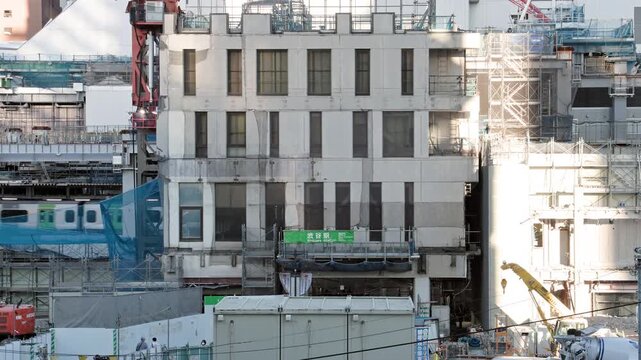 Tokyo Scene :  Reconstruction Work on the Station Building Is Underway, Temporarily Covered in Scaffolding, While a Train Arrives at the Exposed Platforms | Shibuya Station, Tokyo, Japan