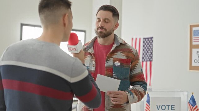 Man wearing voted sticker and holding ballot paper while interviewer points red microphone at his mouth in a polling building with us flag visible; civic duty pride.