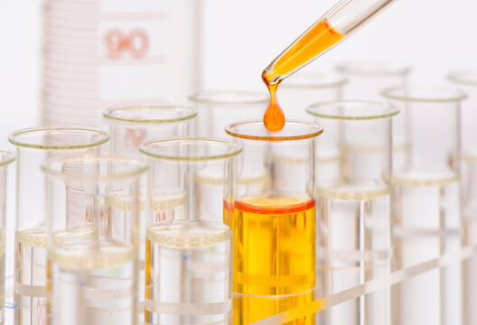 Aus einer Pipette f&auml;llt ein Tropfen gelber Fl&uuml;ssigkeit in ein Reagenzglas in einem Labor