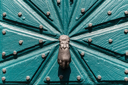 View of an ornate teal wooden door featuring a starburst pattern with metal studs and a hand-shaped iron door knocker in the historic village of Monreal, Rhineland-Palatinate, Germany.