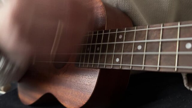 Man strumming ukulele strings close up at home, playing music, rhythm practice, creative hobby activity, musical performance