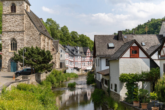 View of historic half-timbered houses and the stone Trinity Church along the Elzbach river under a bright sky Monreal, Rhineland-Palatinate, Germany.