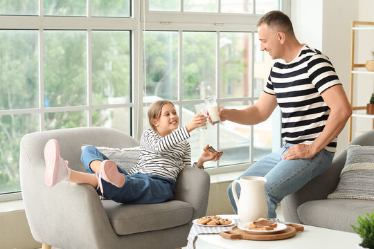 Little girl with her father eating chocolate paste toasts and drinking milk in living room