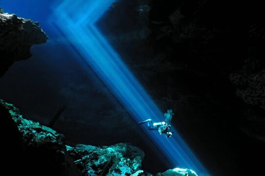 Scuba diver swimming underwater in the sun beams. Large cenote cave with blue light rays and scuba diver.  Explorer diving in the dark cave, travel picture. Cenote and diver