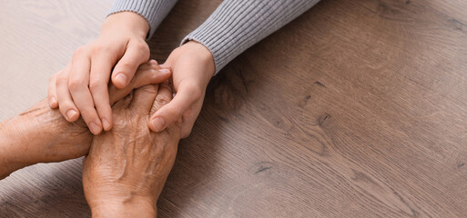 Obraz premium Young woman with grandmother holding hands on table, closeup. Care concept