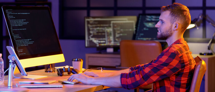 Young bearded programmer working with computer in office at night