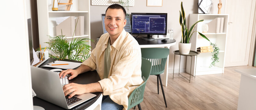 Handsome programmer working with laptop at table in office