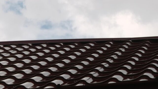 Wet brown metal roof tiles reflecting clouds