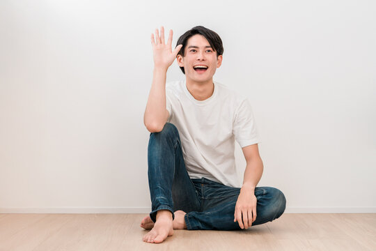 A young Asian man sits cross-legged in the living room and waves (Men's Beauty)