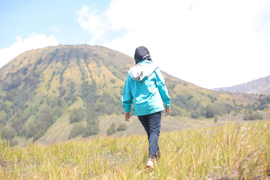 Female traveler walking through green savanna with the majestic Mount Batok Bromo as a backdrop.