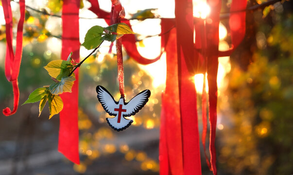 Dove pendant, red ribbons on tree branch, sunny abstract nature background. Christian symbol of Holy Spirit, Holy Trinity Sunday, Pentecost day. Christianity religion, faith in God, Church holiday